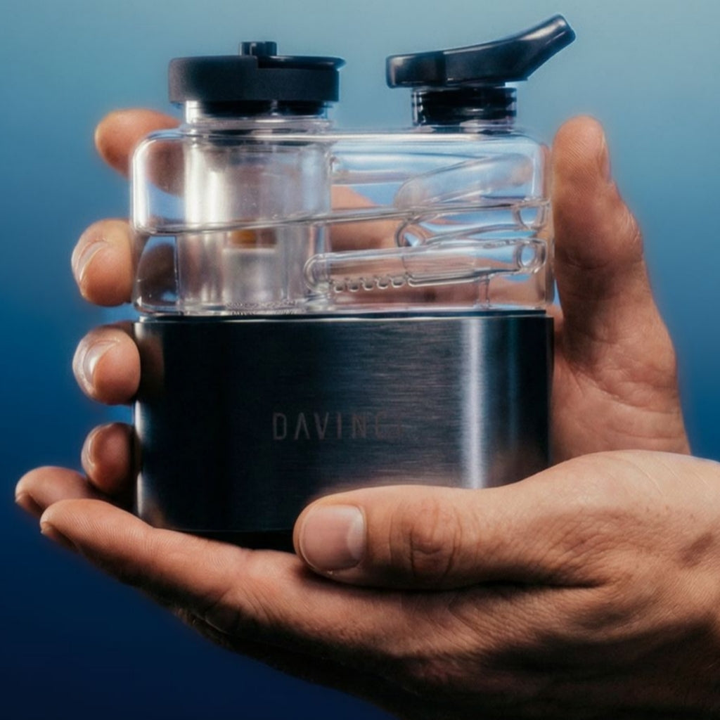 DaVinci EQ E-Rig held in one hand, featuring a clear glass bubbler and a sleek metal base with touch controls.
